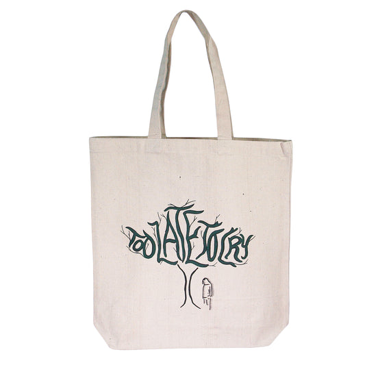 The Too Late To Cry - Natural Tote Bag is a beige canvas tote with two handles, featuring a tree illustration on the front. Green branches spell out "Too Late To Cry" with a simple figure standing beneath the tree.